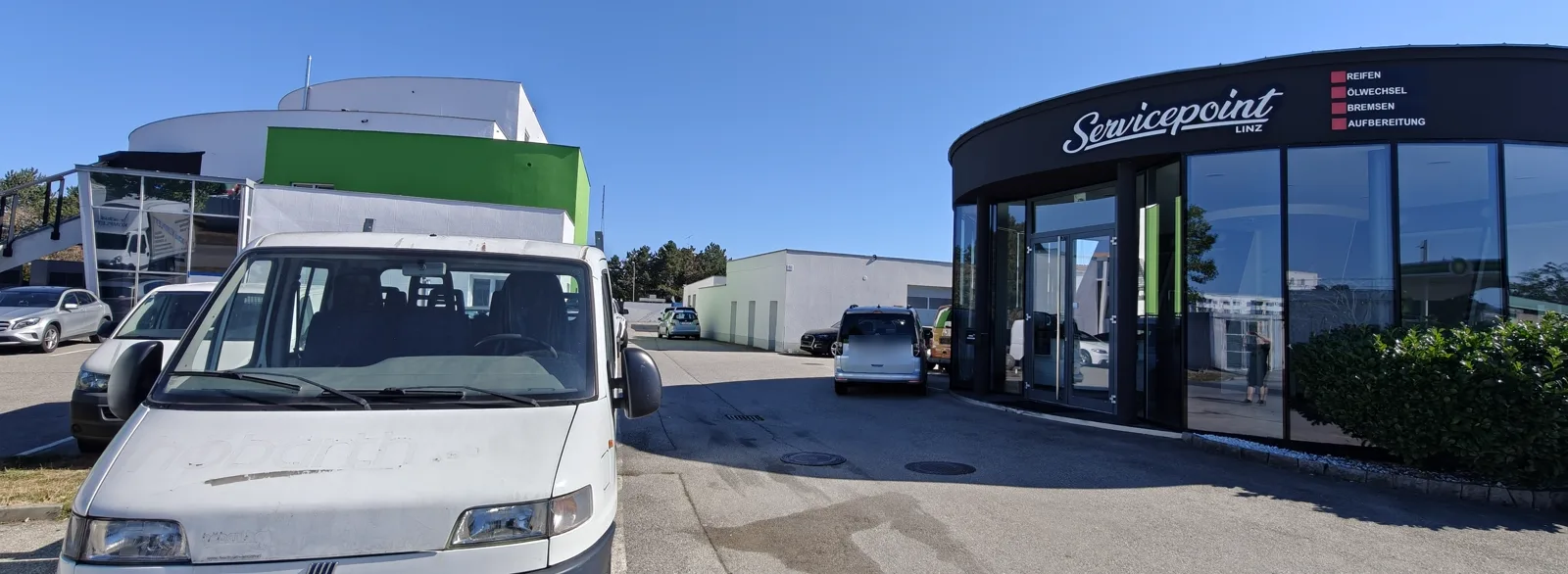 Rechts das schwarze Rundgebäude von Servicepoint Linz, links das grüne Gebäude der Poolhall, dazwischen führt die Einfahrt hinein