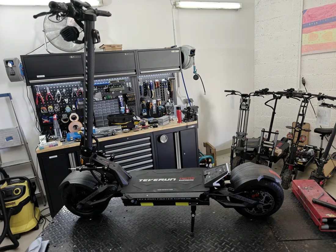 Großer Hochleistungs-Scooter auf der Hebebühne, dahinter Werkzeugwand und weitere Sportgeräte